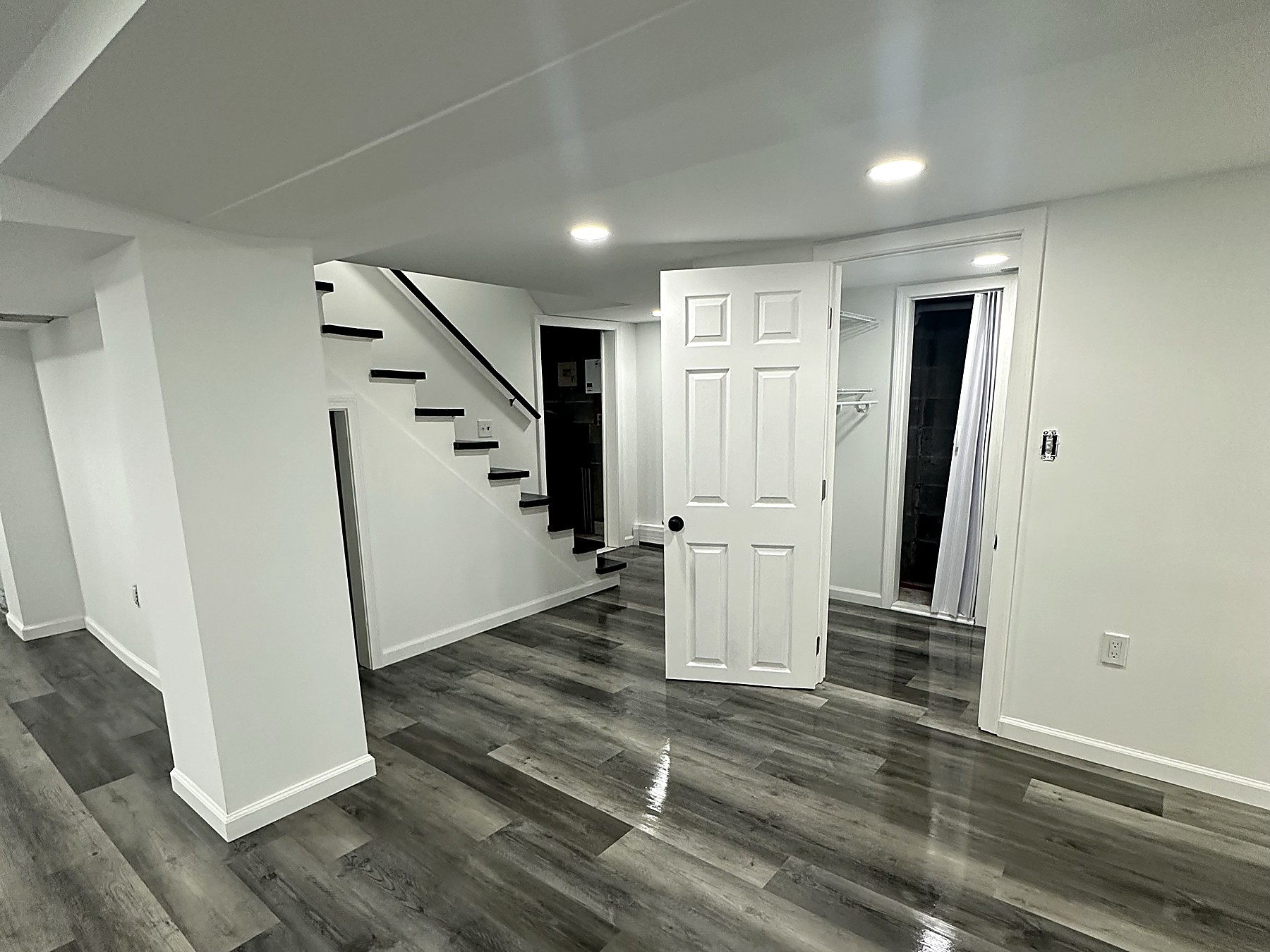 Finished basement in Prospect Connecticut with grey wide-plank vinyl flooring, bright white walls and trim, recessed LED lighting, an open painted stair run, and a new six-panel closet door