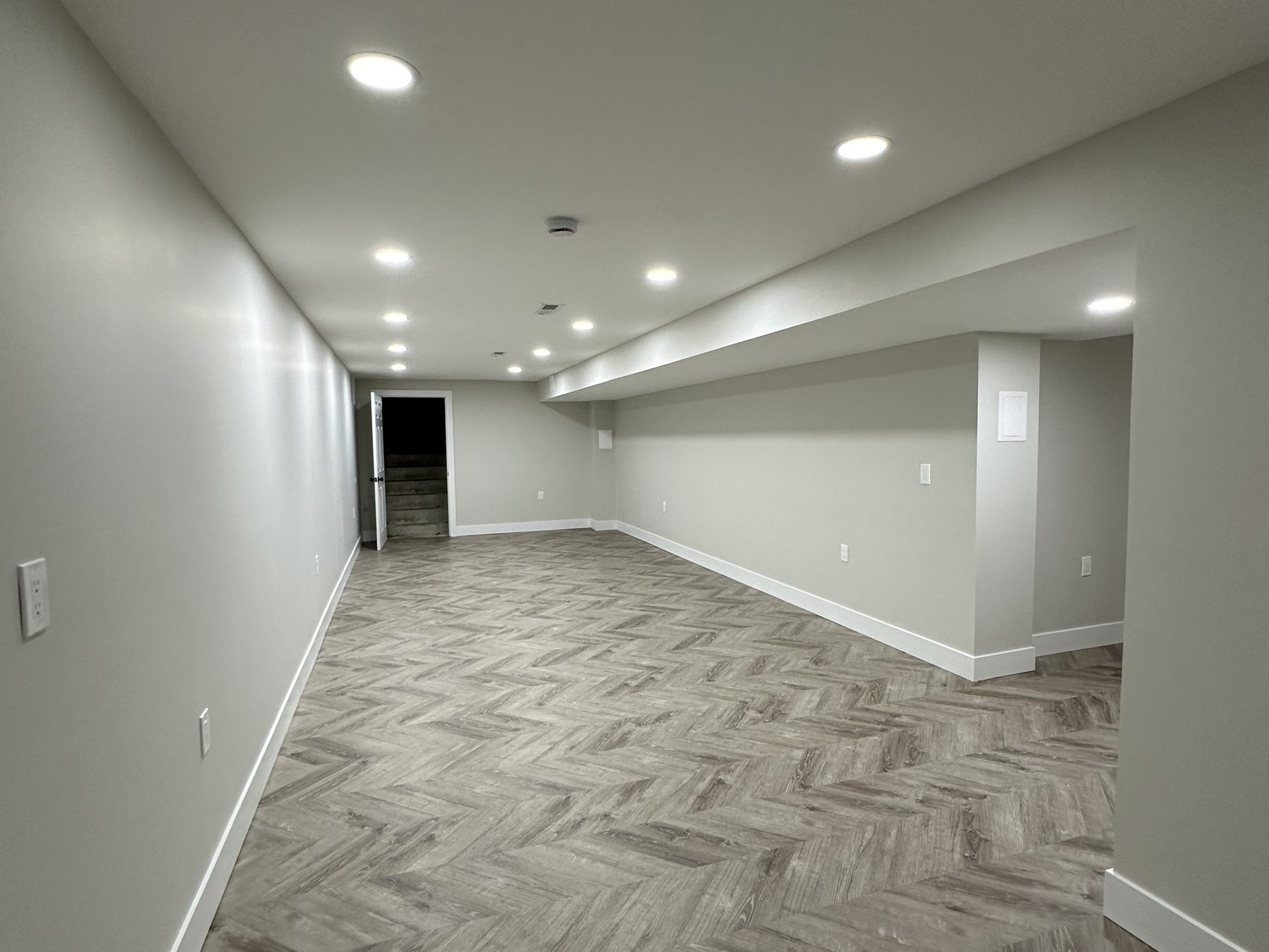 Finished basement in Madison Connecticut with herringbone luxury vinyl plank flooring, white walls, recessed LED lighting, and a soffit built around ductwork